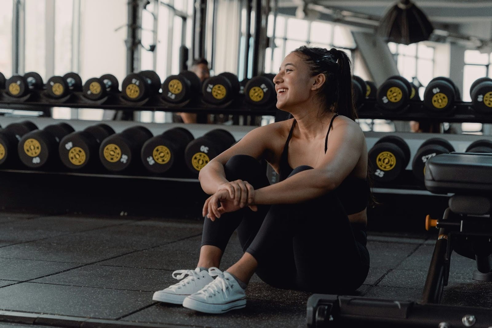 Vrouw in sportkleding zit voor een rek met dumbells
